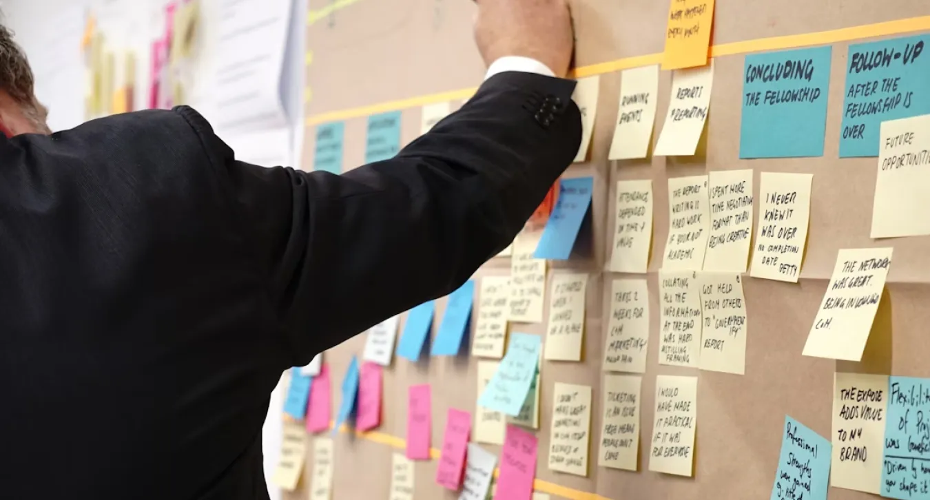A woman working on a board full of sticky notes related to managing ongoing projects