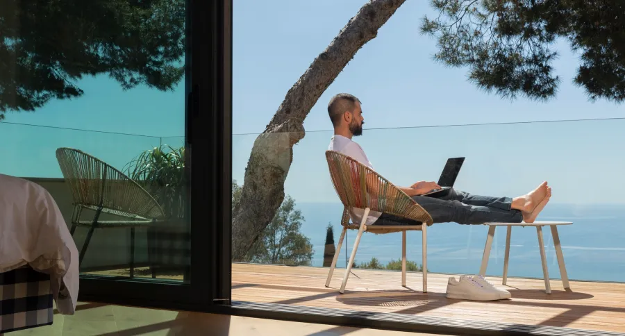 a man sitting in a vacation house's balcony working on a laptop